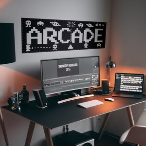 May include: A black desk with a white keyboard, a black computer monitor, a black laptop, a black lamp, and a black speaker. The monitor displays a video editing program with the text "SNOWTRIP HOKKAIDO 2016". The wall behind the desk has a black and white banner with the word "ARCADE" in pixelated letters.