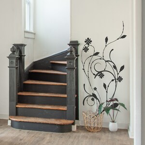 May include: A black wooden staircase with a black railing and a white wall with a black floral design. A wicker basket and a potted plant are on the floor.