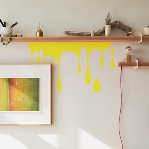 May include: A yellow paint drip wall decal, a wooden shelf with a small light fixture, and a framed picture on a white wall.