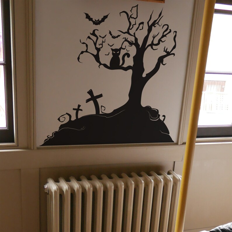 May include: Black and white Halloween wall decal featuring a spooky tree with bats and a cat, and three tombstones. The decal is applied to a white wall above a white radiator.