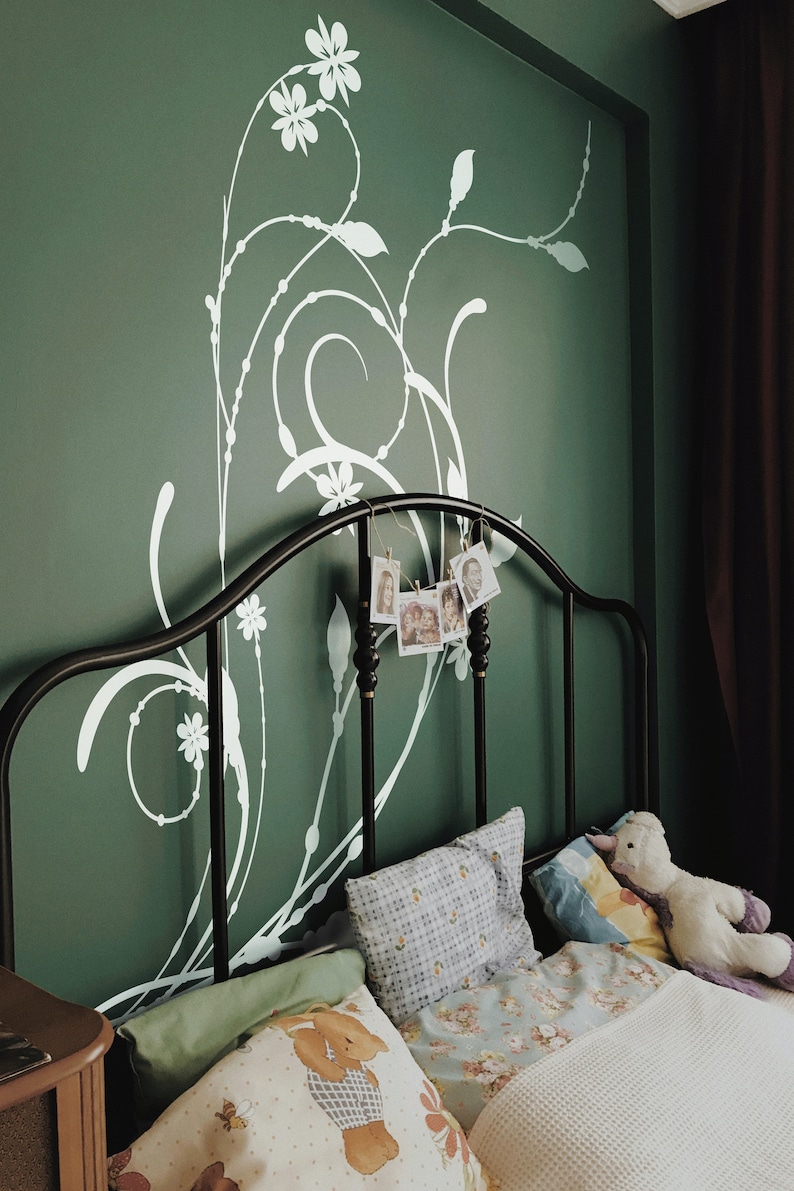 May include: A black metal bed frame with a white floral design on the wall behind it. The bed is made with white and blue patterned bedding and pillows. There are several small framed photos hanging from the bed frame.