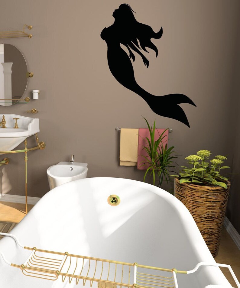 May include: A white bathtub with a gold-colored drain and a gold-colored rack on the side. A black silhouette of a mermaid is on the wall behind the bathtub.