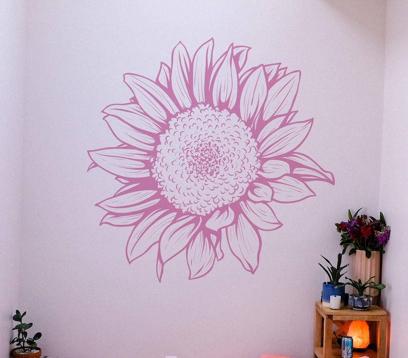 Puede incluir: Una calcoman&iacute;a de pared gr&aacute;fica de girasol rosa y blanco. El girasol est&aacute; dibujado en un estilo realista y detallado.