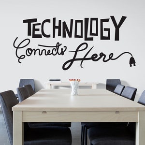 May include: A light wood conference table with black chairs in a meeting room. The wall behind the table has a black and white sign that reads "Technology Connects Here" with a stylized electrical cord and plug.