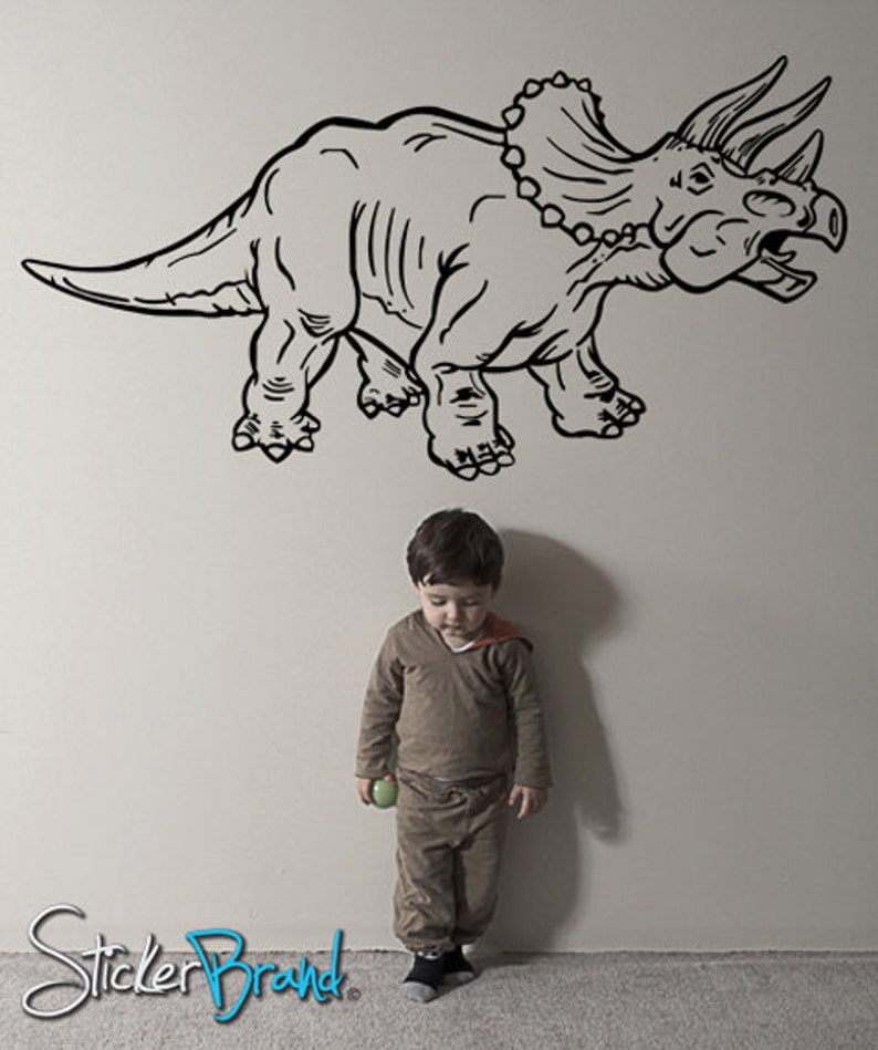K&ouml;nnte beinhalten: Eine Schwarzwei&szlig;-Zeichnung eines Triceratops-Dinosauriers an einer wei&szlig;en Wand. Ein kleines Kind steht vor dem Dinosaurier und h&auml;lt einen gr&uuml;nen Ball.