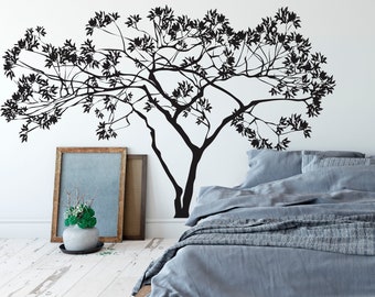 May include: A black silhouette of a tree with branches extending to the left and right, on a white wall behind a gray bed with a gray duvet and pillows.
