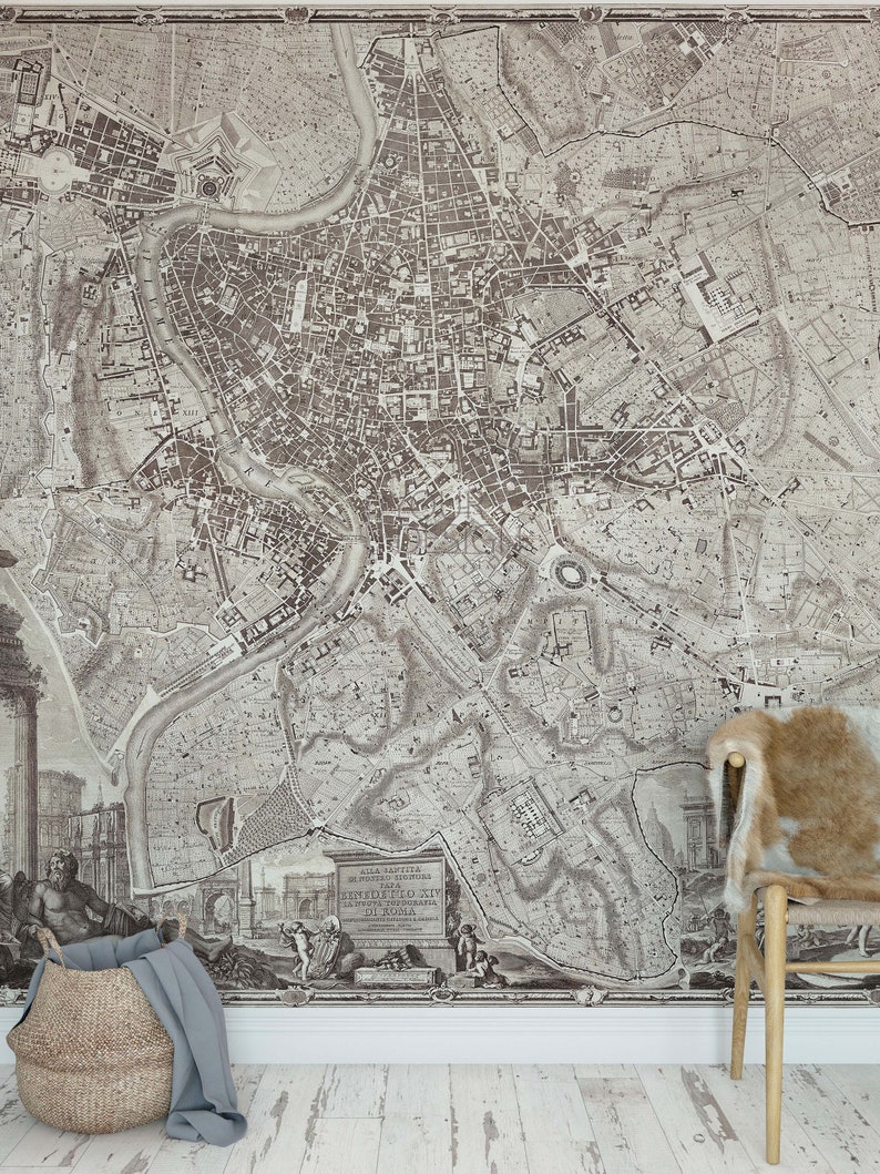 May include: A vintage map of Rome, Italy, printed in black and white. The map shows the city's streets, buildings, and landmarks. The map is framed and hanging on a wall. A wicker basket and a chair with a faux fur cushion are in the foreground.