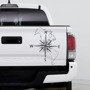May include: A white pickup truck with a black compass and a map of North and South America on the tailgate. The compass points north, south, east, and west.