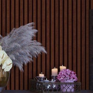 May include: A decorative tray with a woven metal design holds candles and a bouquet of pink flowers. The tray is set against a dark wood wall with a vase of dried pampas grass.