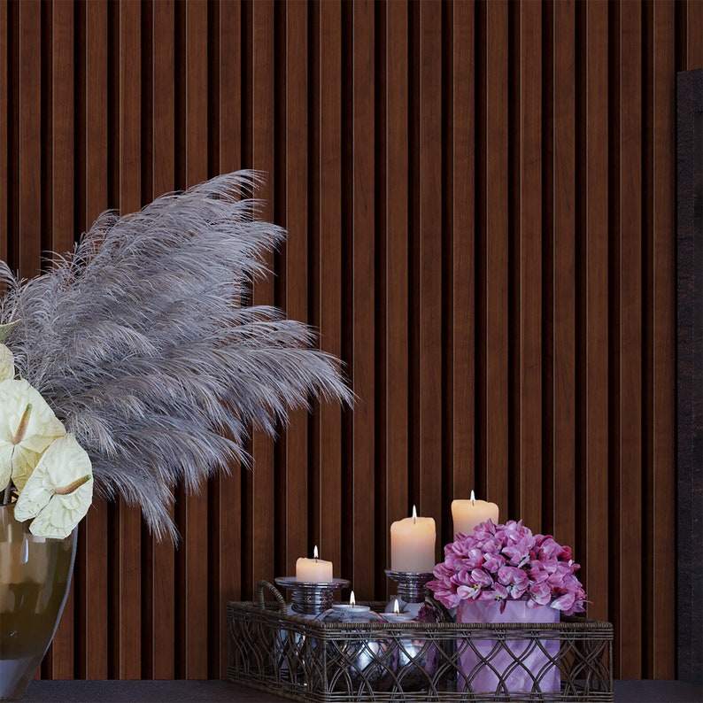 May include: A decorative tray with a woven metal design holds candles and a bouquet of pink flowers. The tray is set against a dark wood wall with a vase of dried pampas grass.
