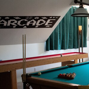 May include: A game room with a pool table, a shuffleboard table, and a black and white wall decal that says "ARCADE".