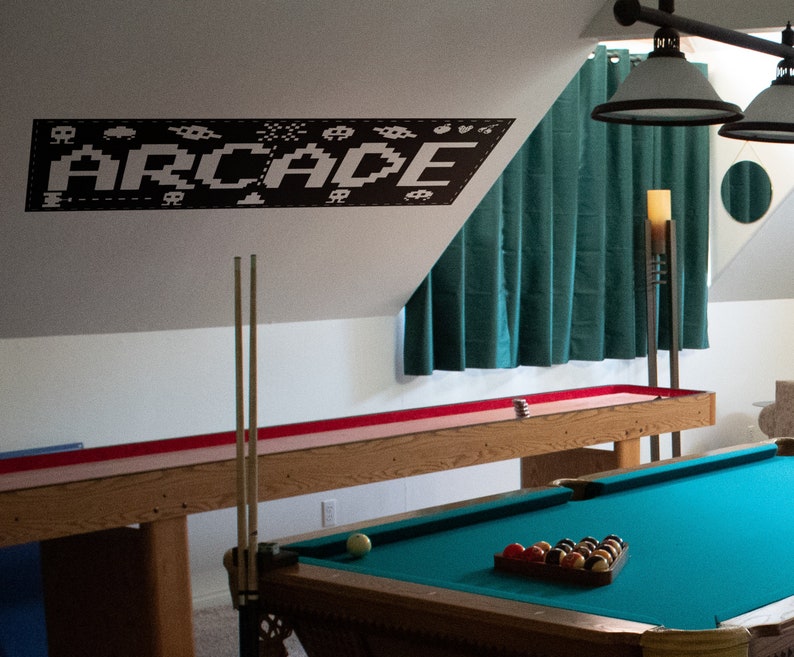 May include: A game room with a pool table, a shuffleboard table, and a black and white wall decal that says "ARCADE".