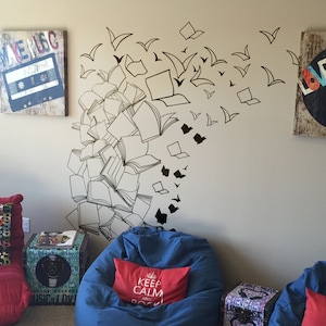 May include: A white wall with a black and white wall decal of books and birds. The decal is in the shape of a cloud. There are two bean bag chairs in the image, one blue and one red. The blue bean bag chair has a red pillow with the text "Keep Calm and Rock On".