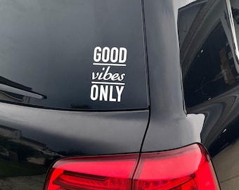 May include: A black car with a white vinyl sticker on the back window that says "GOOD vibes ONLY".