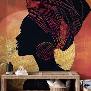 May include: A wall art print featuring a black silhouette of a woman wearing a head wrap and large hoop earrings. The background is a gradient of orange and yellow, with a sun-like design. A wooden bench and decorative items are in the foreground.