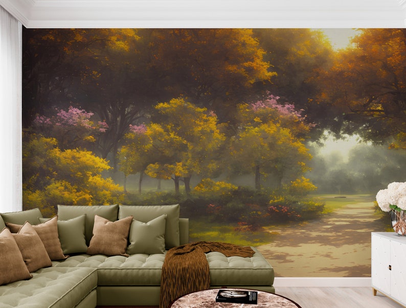 Pode incluir: Um grande mural de parede que retrata uma cena de floresta densa com folhagem amarelo-dourada e verde-escura, flores cor-de-rosa e um caminho iluminado pelo sol. O mural est&aacute; instalado atr&aacute;s de um sof&aacute; de canto verde-s&aacute;lvia com almofadas e manta castanha.
