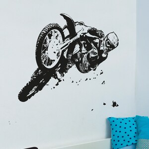 May include: Black and white silhouette of a motocross rider performing a stunt on a dirt bike. The rider is wearing a helmet and goggles. The bike is in mid-air, with the front wheel off the ground. The image is set against a white background.