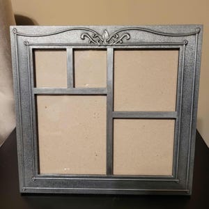 May include: A square multi-opening picture frame with a textured silver finish. The frame features a decorative scrollwork detail at the top center and is divided into four distinct rectangular sections for displaying multiple photographs.