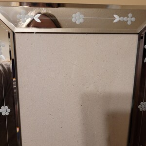 Puede incluir: Un marco de fotos rectangular con una superficie espejada y dise&ntilde;os florales grabados. El marco tiene un borde marr&oacute;n oscuro y un respaldo de color neutro. Los detalles grabados incluyen flores y formas de hojas.