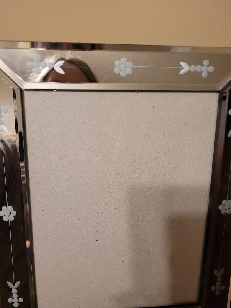 Puede incluir: Un marco de fotos rectangular con una superficie espejada y dise&ntilde;os florales grabados. El marco tiene un borde marr&oacute;n oscuro y un respaldo de color neutro. Los detalles grabados incluyen flores y formas de hojas.