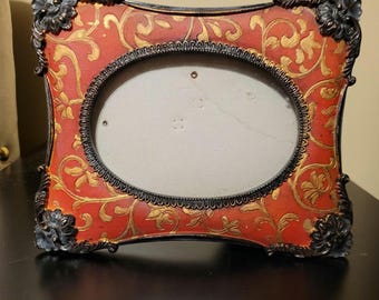 Ornate red and gold photo frame with a baroque-style border and an oval opening.