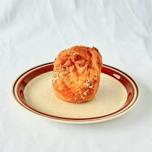 May include: A golden brown pastry with a swirl design and sesame seeds on top, sitting on a brown and white striped plate.