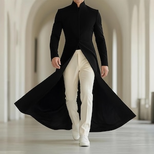 May include: A black, long-line coat with a high collar, worn with cream trousers and white shoes. The coat has a split front, creating a flowing effect. The outfit is suitable for formal events and occasions.