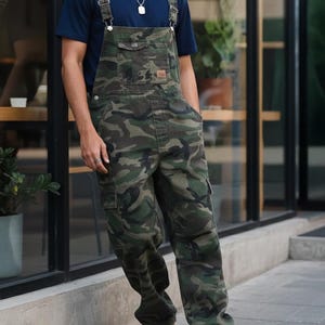 Men's slim-fit camouflage denim bib overalls with adjustable shoulder straps and multiple pockets in an urban streetwear design