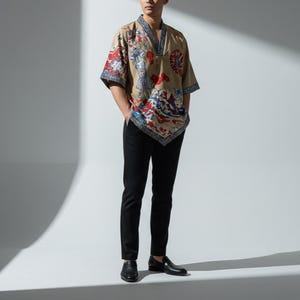 Pode incluir: Uma camisa bege estilo quimono com um design estampado colorido com elementos vermelhos, azuis e brancos. A camisa é combinada com calças pretas e sapatos pretos. A roupa é uma fusão de estilos tradicionais e modernos.