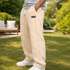 Puede incluir: Pantalones deportivos beige de punto trenzado con cintura con cordón y una pequeña etiqueta negra. Los pantalones se combinan con zapatillas blancas. La palabra "BEIGE" está en la esquina superior izquierda.