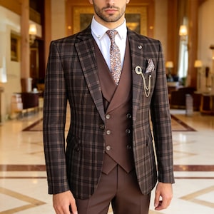 May include: A brown plaid suit with a matching vest and trousers. The suit features a white dress shirt, patterned tie, and a gold chain with a decorative pin. The suit is a classic style for formal events.