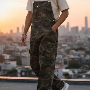 Men's slim-fit camouflage denim bib overalls with adjustable shoulder straps and multiple pockets in an urban streetwear design