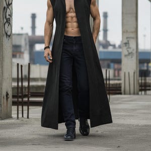 May include: A long, black sleeveless duster coat with a notched collar. The coat is worn with dark blue jeans and black boots. The background shows industrial buildings and concrete structures.