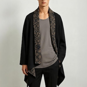 May include: A black open-front cardigan featuring a wide shawl collar with a detailed floral pattern in shades of brown, gold, and dark blue. The garment has long sleeves and a draped hemline, worn over a plain grey tank top and black trousers.