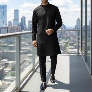 May include: A black long-sleeved tunic with a mandarin collar and button detail, paired with black trousers and black leather loafers. The outfit is worn by a person standing on a balcony overlooking a cityscape.