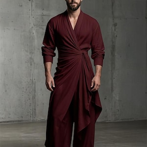 May include: A deep burgundy wrap-style tunic featuring long sleeves, a V-neckline, and a gathered side-tie detail that creates a draped, asymmetrical hemline. The garment is constructed from a solid-colored fabric with a smooth, matte finish.