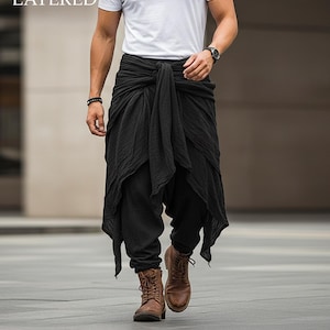 May include: Black layered pants with a draped, asymmetrical design. The pants are paired with a white t-shirt and brown boots. The text "BLACK LAYERED" is visible in the upper left corner.