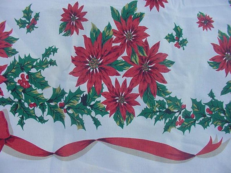 May include: White tablecloth with a red and green Christmas pattern. The pattern features poinsettia flowers, holly leaves, and red berries. A red ribbon with a white border runs along the bottom edge of the tablecloth.