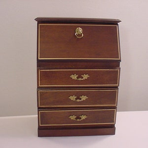 May include: A mahogany wood secretary desk with a lion head pull on the top drawer. The desk has four drawers with brass pulls and gold trim.