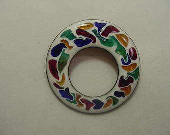 Könnte beinhalten: Eine weiße runde Brosche mit einem farbenfrohen Design. Das Design zeigt abstrakte Formen in Rot-, Blau-, Grün- und Orangetönen.