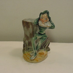 Könnte beinhalten: Eine grüne und braune Keramikfigur eines Kobolds, der auf einem Baumstumpf sitzt. Der Kobold trägt einen grünen Hut und einen weißen Kragen. Die Figur ist im Vintage-Stil und wäre eine großartige Ergänzung für jede Inneneinrichtung.