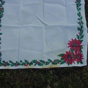 May include: White tablecloth with a green holly and red poinsettia border. The tablecloth is perfect for a Christmas dinner or holiday party.