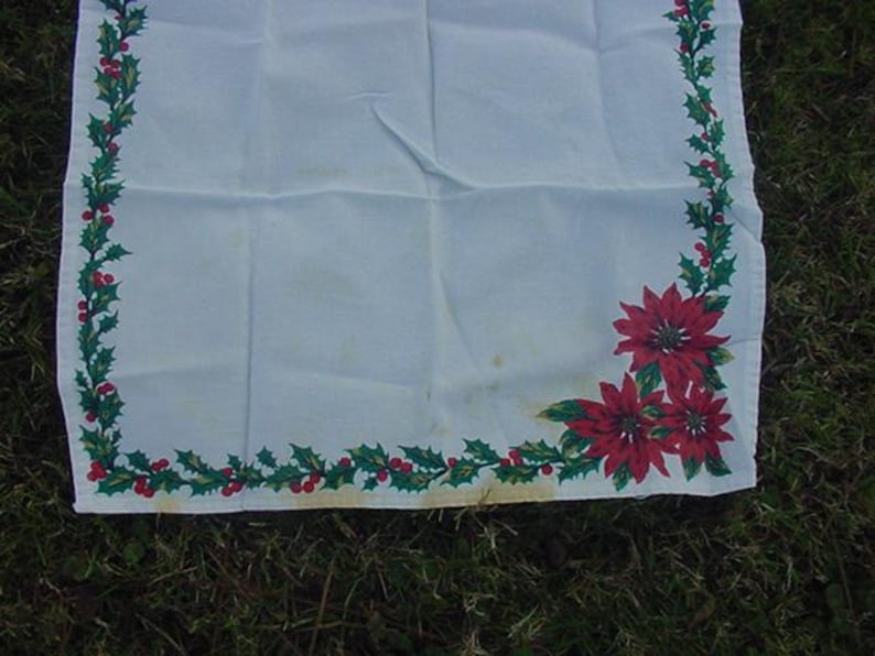 May include: White tablecloth with a green holly and red poinsettia border. The tablecloth is perfect for a Christmas dinner or holiday party.