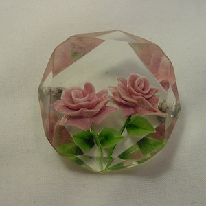 Könnte beinhalten: Eine klare, facettierte Glasbrosche mit zwei rosa Rosen darin. Die Rosen sind dreidimensional und haben grüne Blätter.