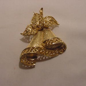 May include: A gold-tone filigree bell brooch with a bow at the top. The bell is made of a delicate, intricate design.