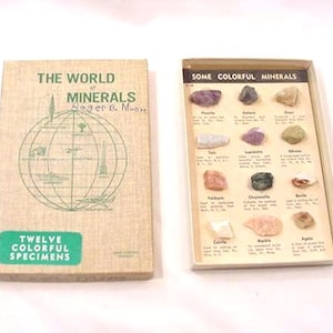 Op de afbeelding: Een vintage educatieve set getiteld "De Wereld van Mineralen" met een doos met twaalf kleurrijke mineraalmonsters. De boekomslag toont een wereldbolafbeelding en de tekst "Twaalf kleurrijke exemplaren". De open doos toont diverse mineraalmonsters.