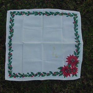 May include: White linen napkin with a green holly and red berry border. The border also features red poinsettia flowers.