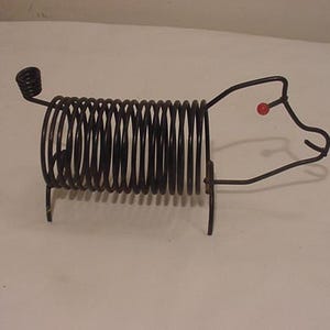 Puede incluir: Un soporte de alambre en forma de cerdo de metal negro con una cuenta roja para el ojo.