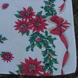 May include: White tablecloth with a red and green Christmas pattern. The pattern features poinsettia flowers, holly leaves, and red bows.