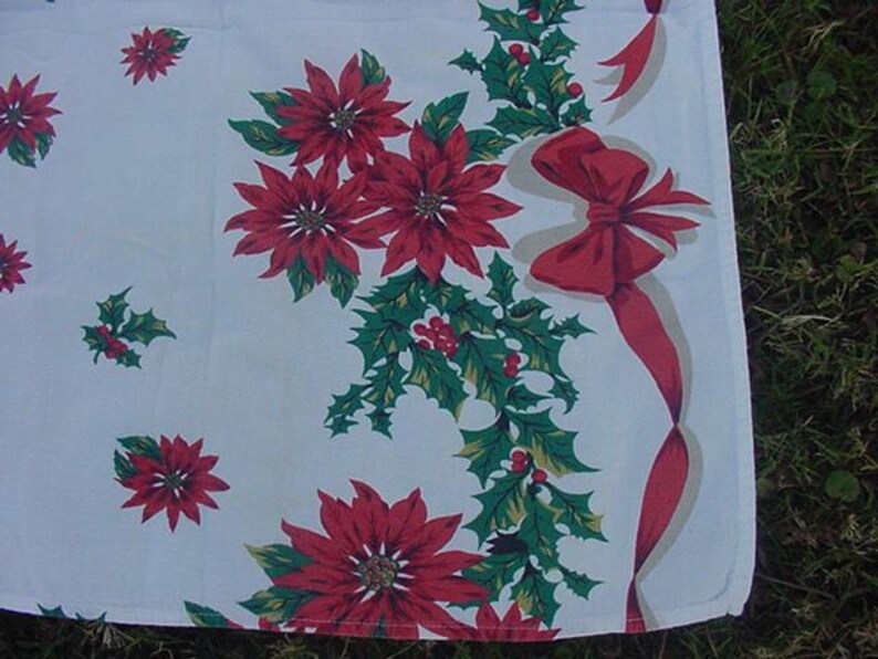 May include: White tablecloth with a red and green Christmas pattern. The pattern features poinsettia flowers, holly leaves, and red bows.